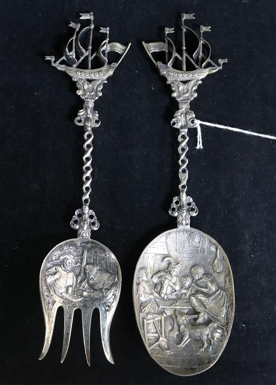 A Dutch embossed silver (.833 min) serving spoon, with tavern scene to bowl and sailing ship finial and a similar fork